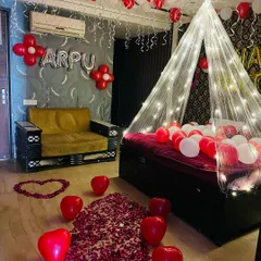 This romantic room setup features a beautiful pathway of rose petals and heart-shaped balloons leading to a bed under a fairy light canopy. I also added a personalized name on the wall with foil letters to make the surprise unique.