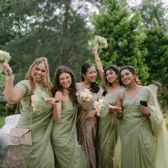 A bride and her bridesmaids, dressed in beautiful matching green sarees, share a happy moment together. Their smiles and bouquets create a vibrant and joyful group portrait.