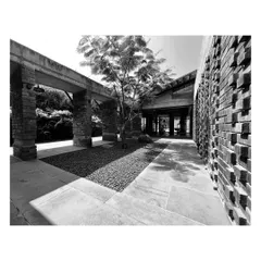A black-and-white photo of a courtyard passage, where the texture of a projecting brick wall contrasts with smooth stone flooring. The play of light and shadow animates the space.