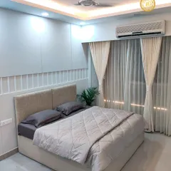 A real bedroom from one of our completed projects, showcasing a minimalist design with a neutral color palette, clean lines, and soft, indirect lighting from the false ceiling. This is simplicity and comfort, perfected.