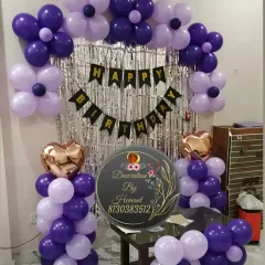 A birthday decoration in shades of purple. This setup features a silver fringe backdrop, a "Happy Birthday" banner, and an arch of dark and light purple balloons, perfect for a celebration in a smaller space.