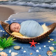 A creative beach-themed setup with the baby sleeping in a boat-shaped prop on a "shoreline" with shells and starfish. This is a great example of a unique, imaginative concept.