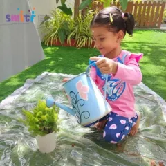A young girl carefully waters a plant with a small watering can. This simple act teaches her responsibility and the importance of caring for living things.
