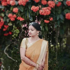 A serene portrait of the bride during her Haldi ceremony, standing before a wall of beautiful orange flowers that complement her sari.