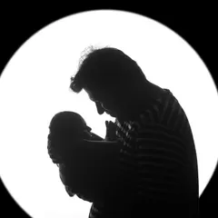 A father's silhouette as he holds his newborn baby up to the light. This black and white portrait is a powerful and artistic representation of a new bond.