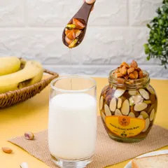 A lifestyle shot showing honey with nuts being added to a glass of milk. This composition suggests a healthy and delicious breakfast or snack option.