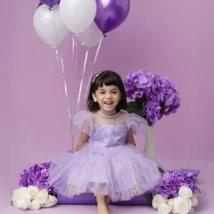Celebrating a third birthday in style. This little girl is all smiles in her beautiful lavender dress, surrounded by matching balloons and flowers.