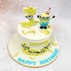 This Minions Banana Cake is full of playful energy, featuring a minion in a party hat, a minion-themed number '3', and lots of edible bananas.