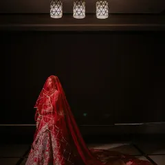 A dramatic, full-length portrait of the bride under soft lighting, her long red veil creating a stunning silhouette. This is bridal elegance at its finest.