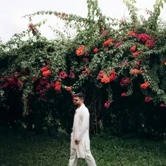A candid shot of the groom walking through a garden. The natural setting and his relaxed posture create an effortless and stylish portrait.