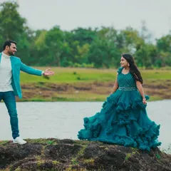 The full view of the coordinated outfits for a lakeside pre-wedding shoot. Her flowing teal gown and his bright blazer make a statement against the natural backdrop.