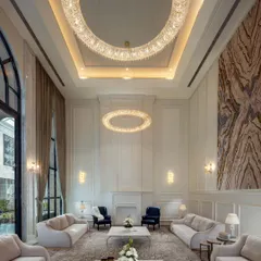 This formal drawing room in The Grand Alabaster is a showcase of neoclassical luxury. The double-height space is anchored by two large, ring-shaped crystal chandeliers and a monumental art piece, creating an environment of pure sophistication.