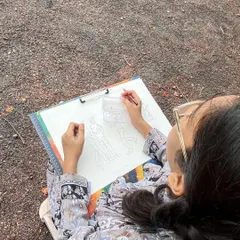 An over-the-shoulder view of a student mapping out the basic shapes and poses of people in the park. This initial step is crucial for getting the composition right before adding details.