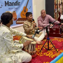 A live performance setup with a student singing, accompanied by his gurus on tabla and harmonium. This is the traditional Guru Shishya Parampara we nurture in our mehfils.