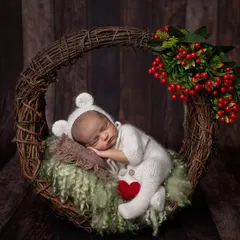 A cozy winter-themed shot with a baby in a white bear onesie, nestled in a wreath with festive red berries. The little red heart adds a pop of color and love.