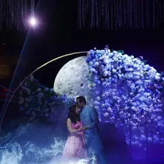 A magical moment as the couple shares a kiss under a stunning floral moon installation, part of our 'Starry Night' engagement theme.