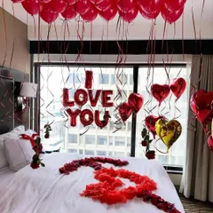 This is our classic romantic room decoration, perfect for proposals and anniversaries. The setup includes a ceiling filled with red balloons, 'I LOVE YOU' foil letters above the bed, and heart-shaped balloons framing the window view.