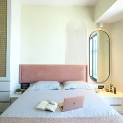 A contemporary bedroom where a pink upholstered headboard is flanked by an arched, fluted wall panel and an elegant oval mirror, creating a soft, symmetrical, and stylish look.