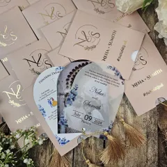 A truly unique fan-shaped invitation that combines modern materials with a playful format. This design features a translucent acrylic card with a delicate blue floral print, attached to a blush pink sleeve with a gold tassel. The sleeve is personalized with the couple's monogram in gold foil.