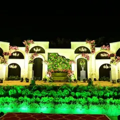 An elegant reception stage with a European architectural feel. The white facade with arched niches, mini chandeliers, and delicate pink floral arrangements creates a sophisticated and romantic backdrop.