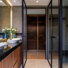 This view showcases the smart layout with a clear division of wet and dry zones. The dual vanity with vessel sinks is separated from the shower and dressing area by sleek, black-framed glass doors.
