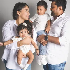 A candid and happy studio portrait of a family of four. The parents hold their two young children, all sharing a moment of connection and joy.