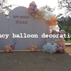 A large outdoor backdrop for a birthday party on a lawn. The setup includes custom arched panels and a balloon garland in a muted, elegant color palette.