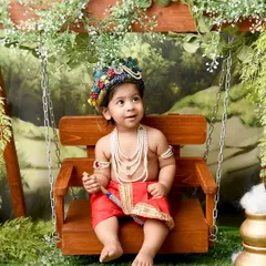 Looking up to the heavens, this little Krishna sits peacefully on a swing. The soft, painterly backdrop and traditional attire create a serene and beautiful image.