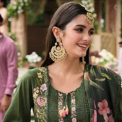 A candid shot of a model smiling, wearing large gold chandbali earrings and a matching maang tikka. These are perfect for a sangeet or mehendi look.