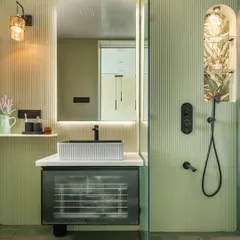 This master bathroom is a serene oasis, featuring soft green fluted walls and a unique shower niche with botanical wallpaper. The floating vanity with a reeded glass front and the modern black fixtures add a touch of contemporary elegance.