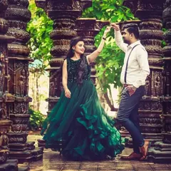 A playful moment between a couple during their pre-wedding shoot. The woman is wearing a gorgeous dark green ruffled gown, perfect for a dramatic, architectural setting.