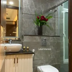 A compact and elegant bathroom design. The space features grey marble-finish tiles, a vessel sink on a white vanity, and a simple glass partition for the shower area.