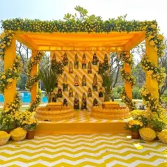 A classic Haldi ceremony setup, featuring a mandap draped in yellow and adorned with fresh flowers. The chevron-patterned floor and traditional seating create a perfect blend of modern design and timeless tradition.