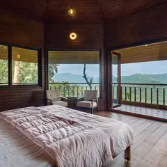 This bedroom opens onto a private balcony with panoramic views of the hills. The use of wood paneling on the walls and floor creates a cozy, cabin-like feel, perfect for a mountain retreat.