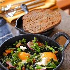 Our Green Shakshuka, a vibrant and healthy dish with eggs baked in a savory green sauce of herbs and vegetables, served in a cast-iron skillet with a side of sourdough.