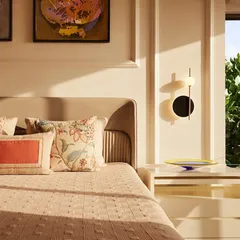A close-up of a bedroom in one of the apartments, where soft, natural light highlights the textures of the bedding, wall molding, and a contemporary bedside lamp.