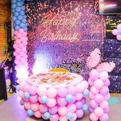 A beautiful butterfly-themed birthday setup. The cake table is wrapped in pastel pink and blue balloons, complemented by a shimmering backdrop and large butterfly accents for a magical feel.
