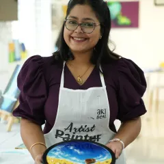 A participant proudly holds up her completed resin beach art, featuring realistic waves, a sandy shore, and a tiny boat. It’s amazing what you can create in just one session, even with no prior experience.