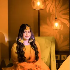 A serene portrait of the bride during her Haldi ceremony. The warm, yellow tones of her outfit and the soft lighting create a beautiful glow, highlighting her floral jewelry and joyful anticipation.