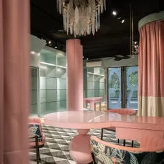 Inside the fashion studio, bold pink columns and custom-designed tables create sculptural forms within the space. The design balances open areas for display with intimate zones for client consultations, all unified by a distinct color palette.