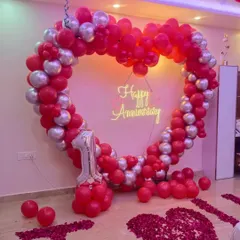 Apni pehli anniversary ko khaas banane ke liye humne yeh red aur silver chrome balloons ka heart shape frame taiyar kiya hai. Beech mein 'Happy Anniversary' ka neon sign iski sundarta aur badha raha hai.