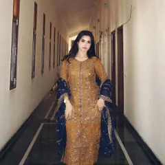 A direct, full-length shot of a mustard and blue ethnic suit by Asim Jofa. The long corridor provides a clean, symmetrical backdrop that puts the entire focus on the detailed craftsmanship of the wedding wear.