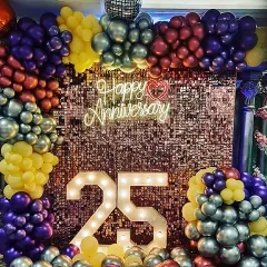 This vibrant 25th anniversary photo booth features a sparkling sequin wall and a multi-colored balloon arch. The large light-up numbers and a central neon sign create a fun and glamorous spot for taking pictures.