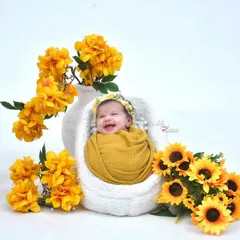 Capturing a precious, happy smile from a newborn baby swaddled in a yellow wrap. The scene is decorated with bright sunflowers and yellow flowers for a cheerful and sunny portrait.