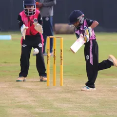 An action shot from a U-10 match, with a young batter playing a shot as the wicketkeeper watches closely. This highlights our focus on grassroots cricket.