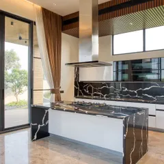 This modern kitchen combines functionality with high-end aesthetics. A statement island with a waterfall countertop in black marble serves as the centerpiece, complemented by sleek white cabinetry and a professional-grade chimney hood for a clean, open feel.