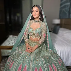 A breathtaking bridal portrait. The hair is styled in soft, open waves, tucked behind one ear to showcase the earrings, while the other side frames the face. A delicate maang tikka and sheer dupatta complete this modern bridal look.