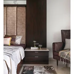 This view highlights the complete bedroom composition, from the plush upholstered headboard and dark wood paneling to the cozy armchair in the corner. A patterned rug adds texture and defines the sleeping area.