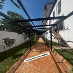 A view from inside the metal pergola at the Partha construction site, looking down the long, paved walkway bordered by a new lawn.