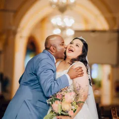 A joyful and candid moment between the bride and a family member, likely her father, sharing a laugh and a kiss on the cheek in the church.